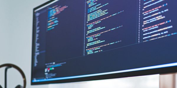 Um monitor com códigos na tela sobre uma mesa de madeira.